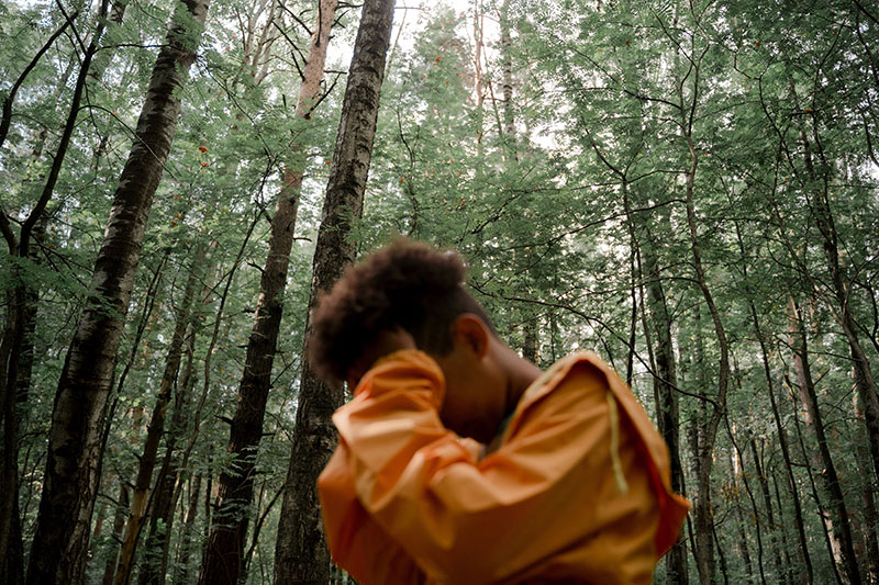 A poignant photograph depicting a teenage boy standing amidst a forest, his hands cradling his head.